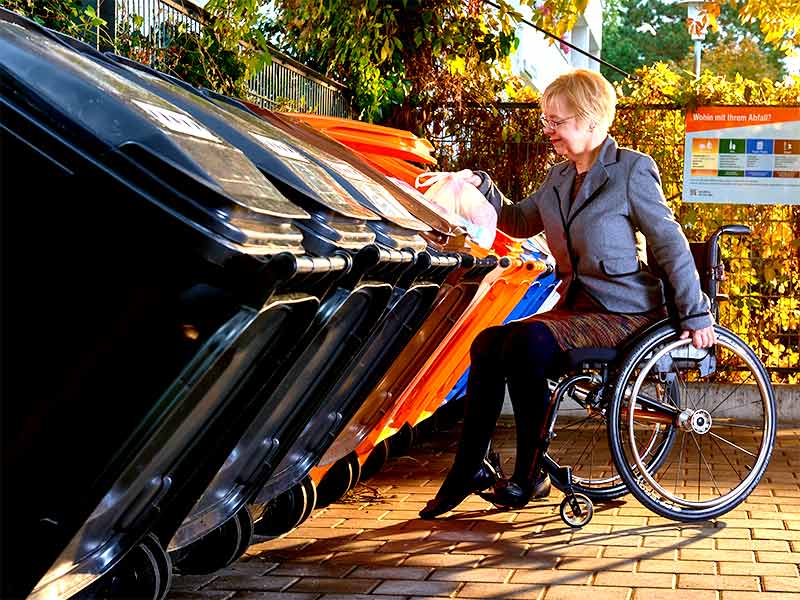 Rollstuhlfahrerin bei der Abfallentsorgung