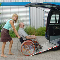 Person schiebt einen Rollstuhl über eine Rampe in einen Bus