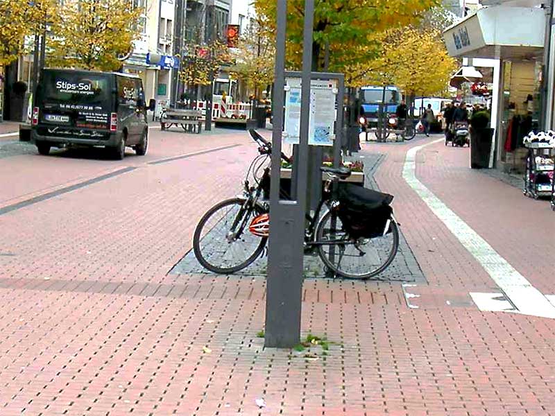 Fahrrad auf einem Abstellplatz in einer Fußgängerzone, an dem ein Leitsystem vorbei führt