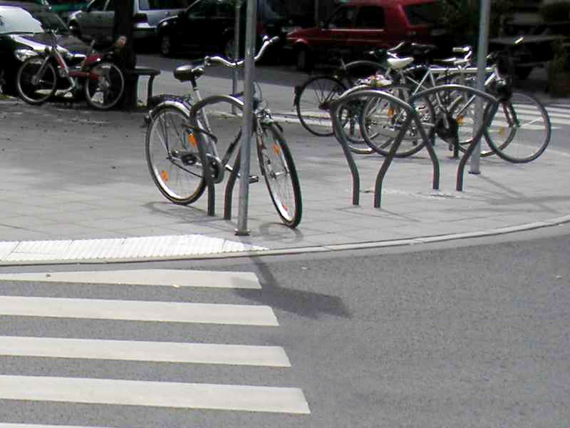 Direkt neben der Rippenplatte einer Fußgängerüberquerung steht ein Bügel, an dem ein Fahrrad angeschlossen ist