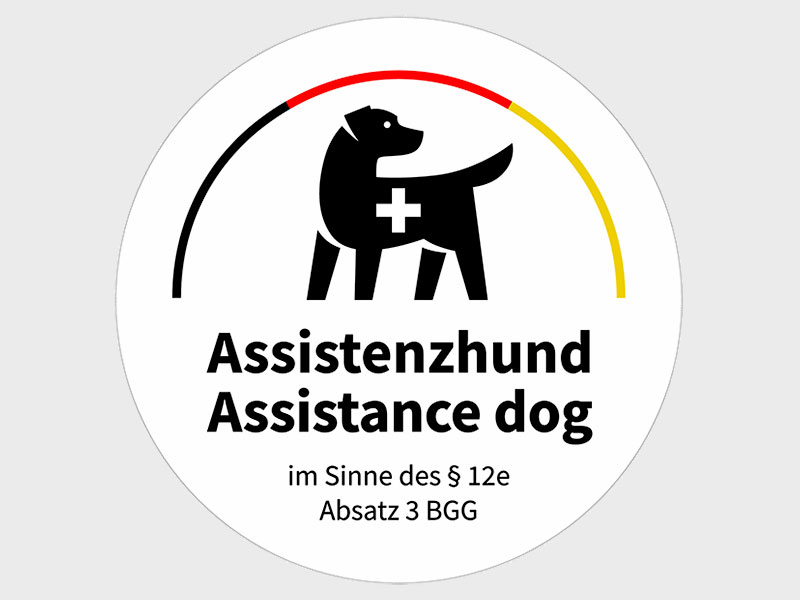 Kennzeichen aus der Assistenzhundeverordnung - ein Hund daüber ein Halbkreis in schwarz, rot, gold und darunter der Schriftzug Assistenzhund im Sinne des § 12e Absatz 3 BGG