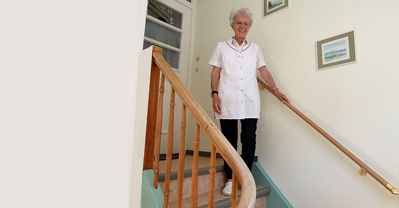 Frau steht auf der letzten Stufe einer Treppe und hält sich am Handlauf fest