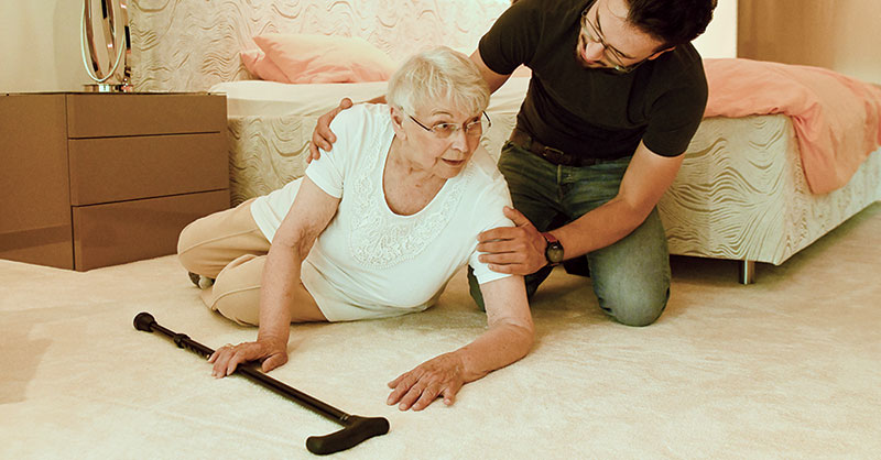 Ein Mann hilft einer Seniorin, die im Schlafzimmer gestürzt ist