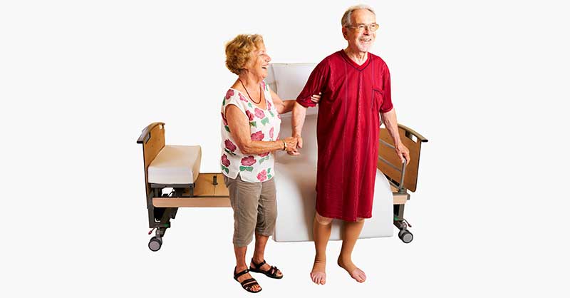 ein älteres Ehepaar läuft gemeinsam lachend und Hand in Hand vor einem Aufstehbett