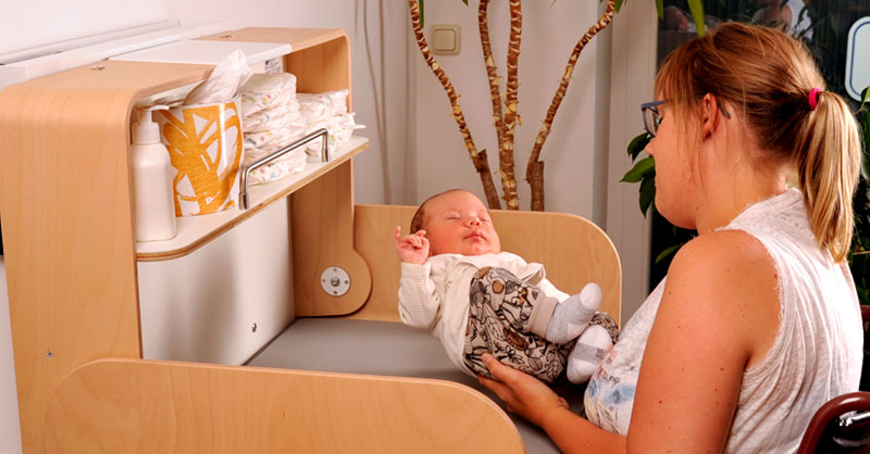Rollifahrerin legt Säugling auf Wickeltisch
