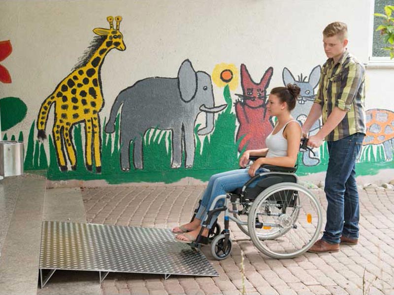 Junge schiebt ein Mädchen im Rollstuhl eine Keilbrücke hinauf