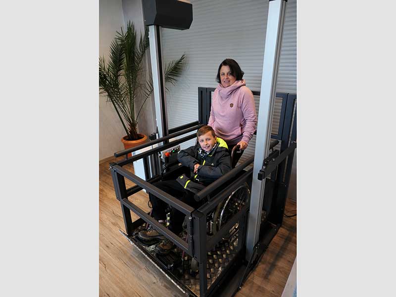 Plattformlift im Wohnraum mit einem Kind im Rollstuhl und einer Muter dahinter