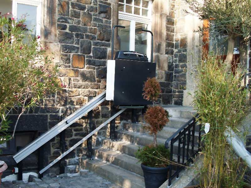 Platzsparend zusammengeklappter Treppenplattformlift EA7 an Außentreppe eines Feldsteinhauses