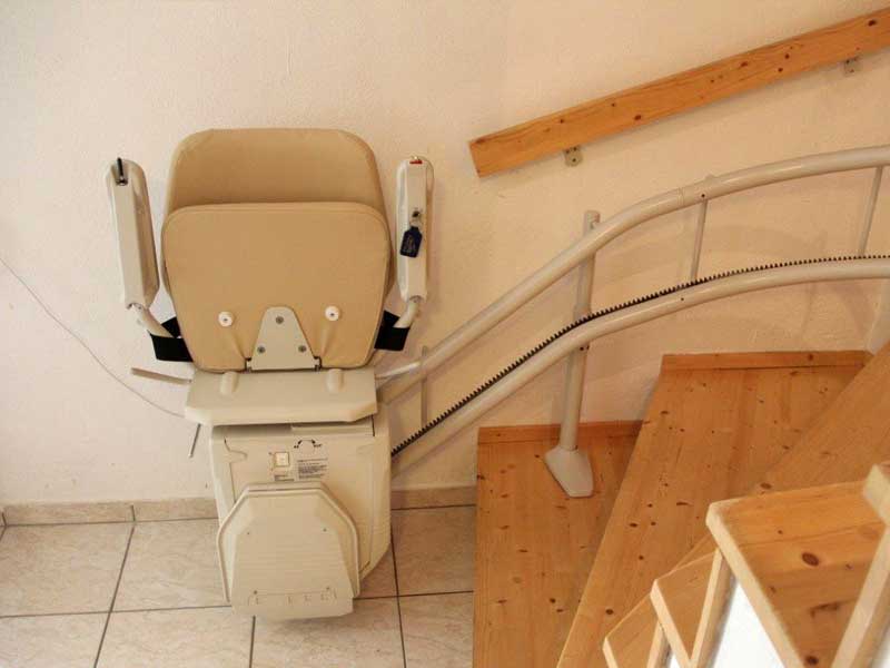 Treppensitzlift mit hochgeklappter Sitzfläche und Armlehnen am Treppenfuß