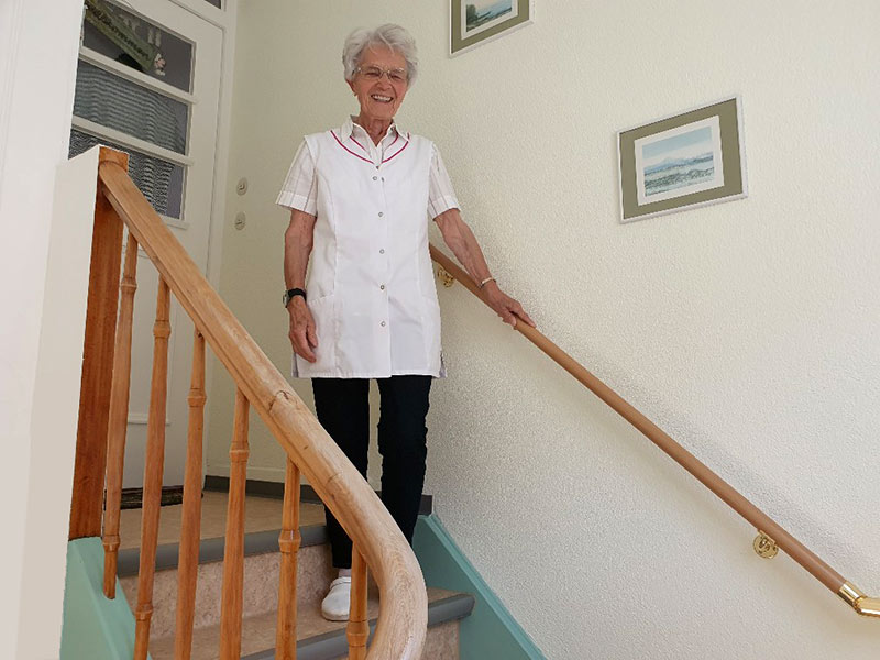 Frau steht auf der letzten Stufe einer Treppe und hält sich am Handlauf fest