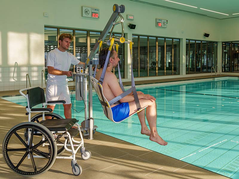 Bademeister nutzt Lifter, um eine Person ins Schwimmbecken zu transferieren