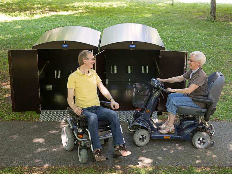 Abstellboxen-Einheit im Park mit Nutzern von Rollstuhl und Mini-Scooter