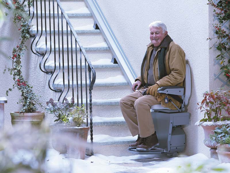 ein älterer Mann benutzt den Außenlift auf einer schneebedeckten Treppe