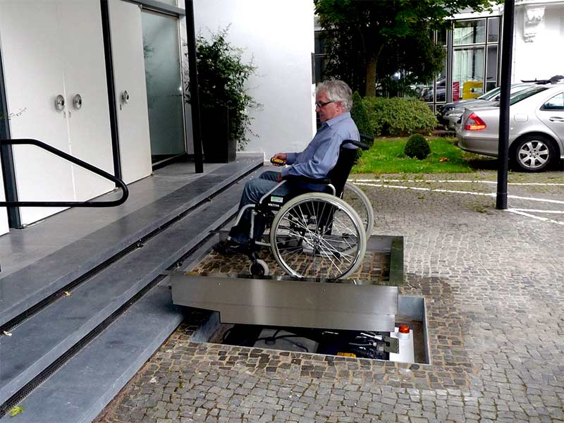 Hubbühne hebt Mann im Rollstuhl über Eingangstreppe