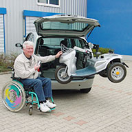 Person befördert mit einer Fernbedienung einen Rollstuhl in den Kofferraum