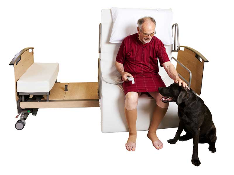ein älterer Mann sitzt auf dem AUfstehbett, was sich in STützposition befindet und streichelt seinen Hund