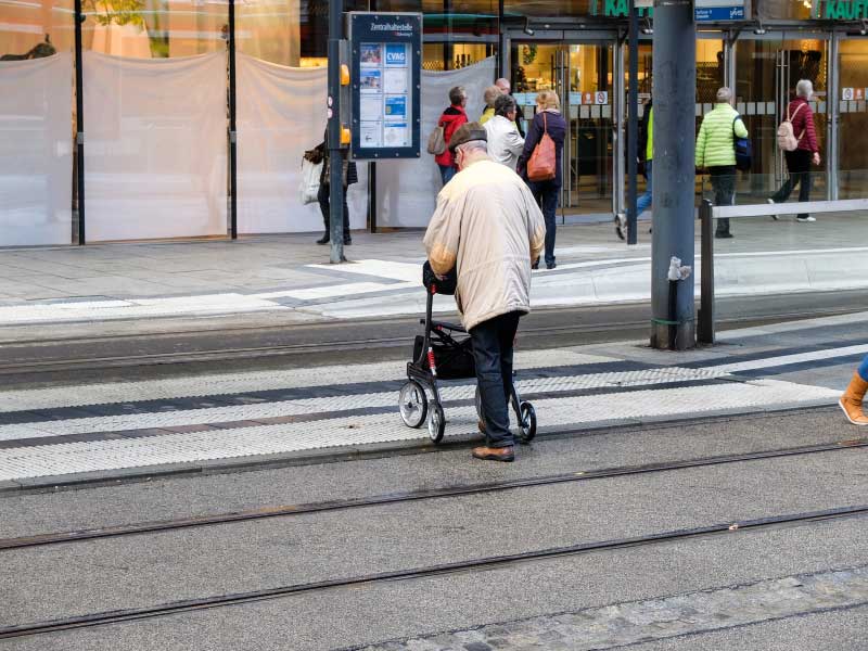 Senior mit Rollator überquert Gleisanlage an Fußgängerquerung