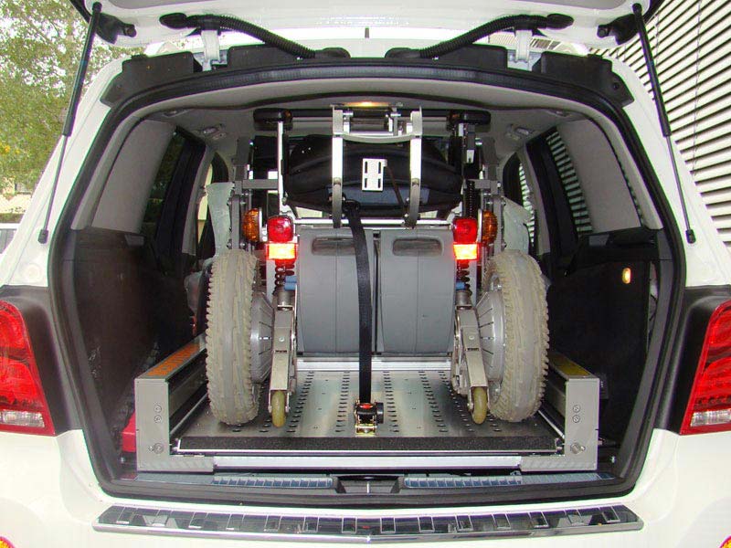 Elektrorollstuhl steht auf der Hebeplattform des Scooterboy Ladesystems in Kofferraum eines weißen Mercedes