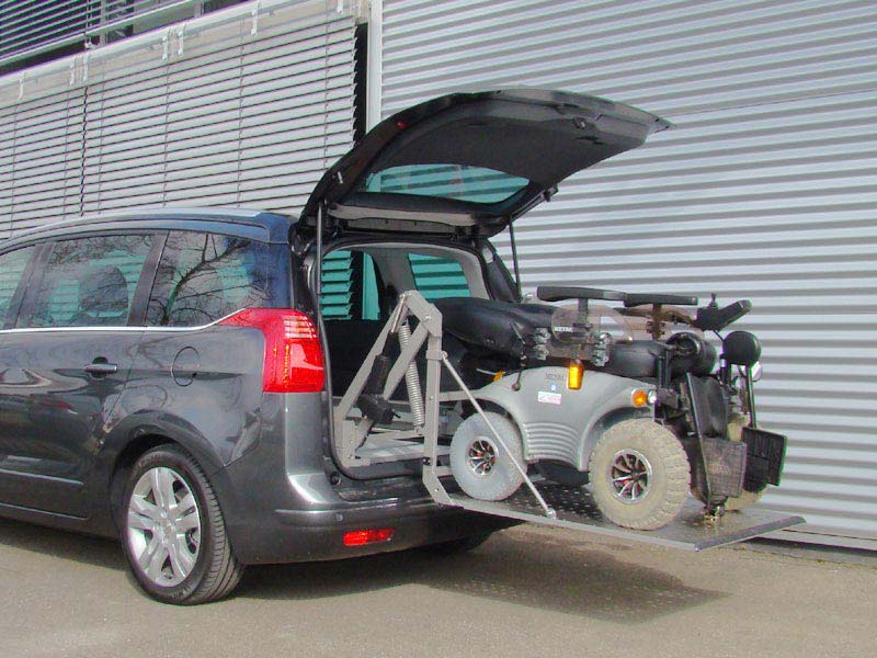 Scooterboy Ladesystem verlädt Elektrorollstuhl in das Heck eines blauen Peugeot Kombi
