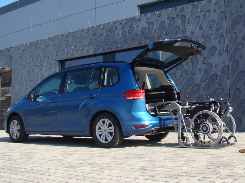 Rollstuhlhebelift hebt Elektrorollstuhl in Heck eines VW Van