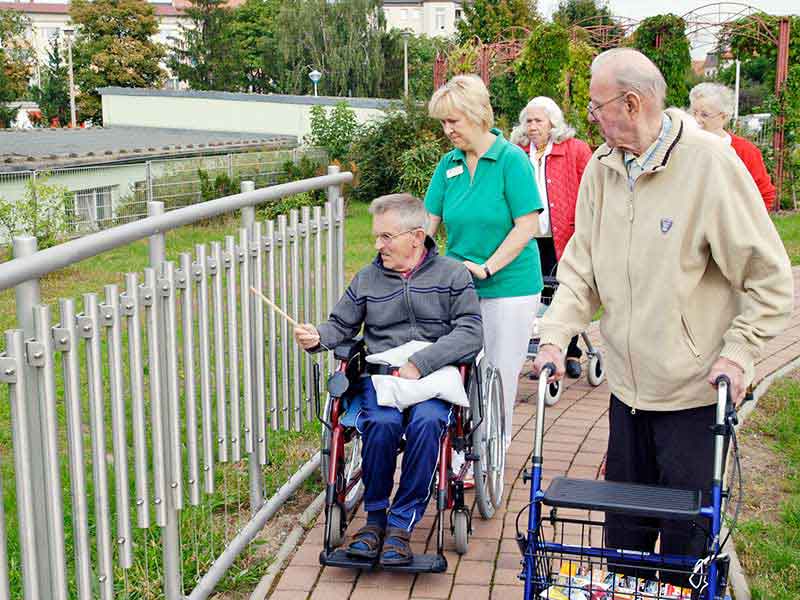 Gruppe Älterer mit Rollstuhl und Rollator am Klangzaun