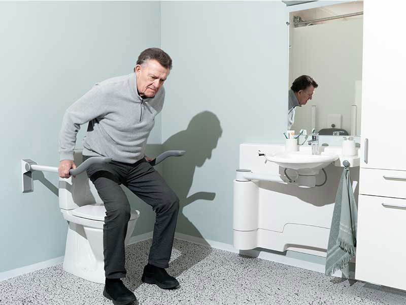 Mann erhebt sich vom WC mit Hilfe von Toilettenst&uuml;tzgriffen