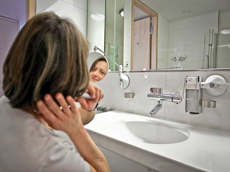 Frau schaut in den Spiegel und benutzt den Spender am Waschbecken