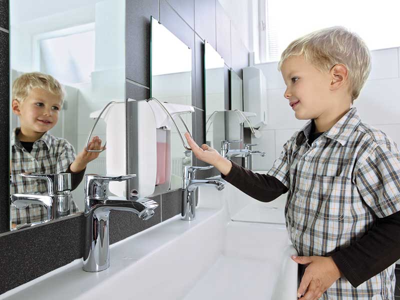 Junge bedient Seifenspender im Waschraum