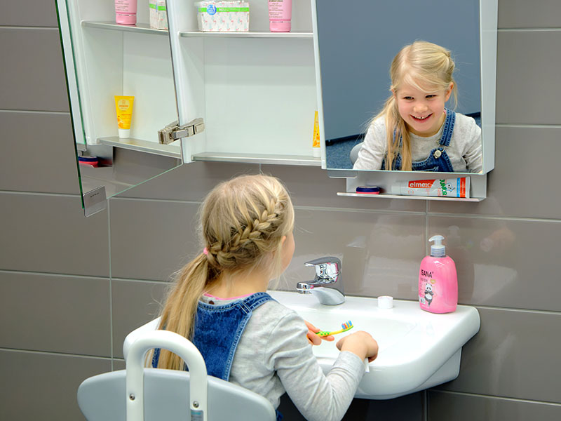 Kind putzt sich vorm Waschbecken und kann sich im Spiegelschrank sehen