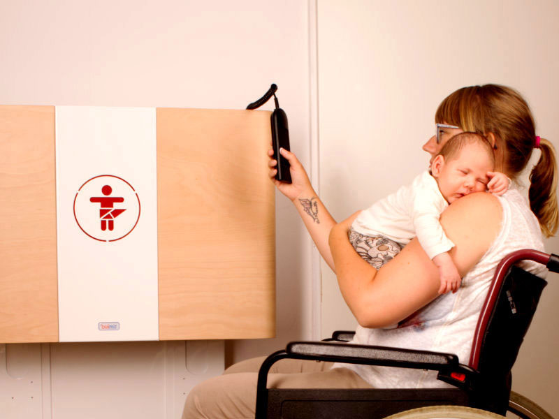Frau im Rollstuhl und Kind auf dem Arm greift zur Fernbedienung