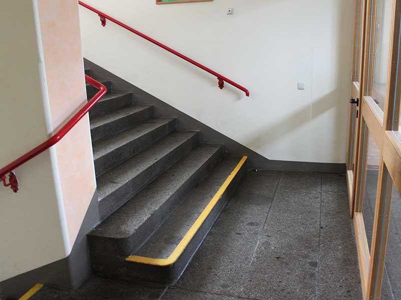 kontrastreiche Handläufe und Stufenmarkierung an einer Treppe in einer Schule