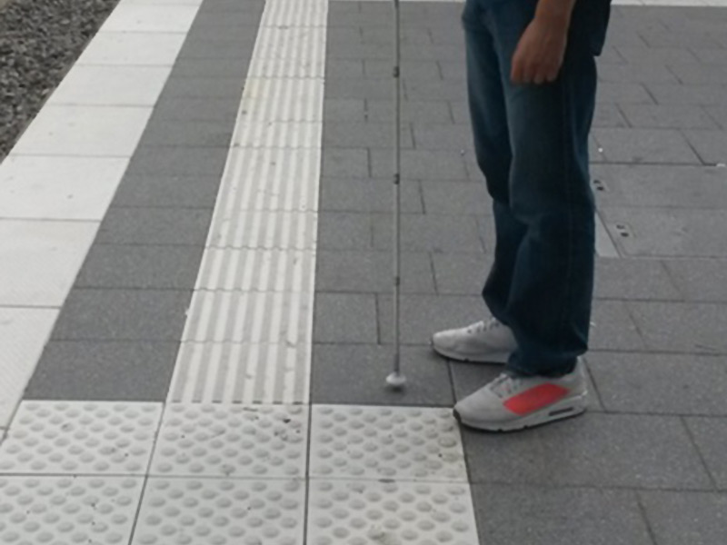 blinder Mann wartet am Bahnsteig auf seine Bahn