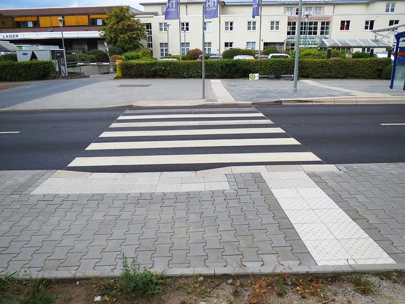 Ein Zebrastreifen der über die Straße führt mit einem Leitsystem für sehbehinderte Menschen auf dem Boden
