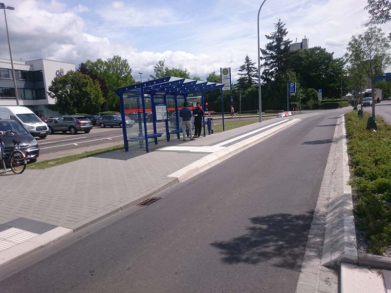 Eine Bushaltestelle an einer Straße mit einem breiten weißen Leitsystem für sehbehinderte Menschen auf dem Boden