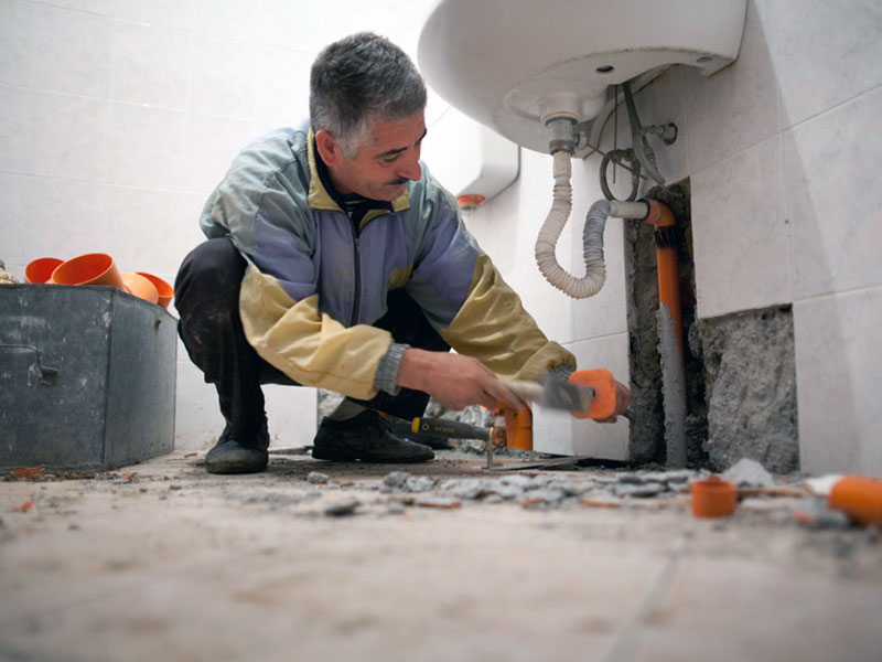 Handwerker verlegt eine Wasserleitung in der Wand unter einem Waschbecken