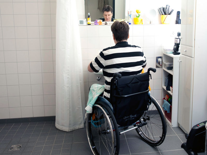 Rollstuhlfahrerin im Bad vor einem zu hoch angeordnetem Spiegel.